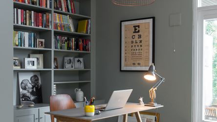 Bildet viser et lite hjemmekontor laget til i et ledig hjørne i en leilighet. En pult med PC og en lampe lyser ut i rommet. 