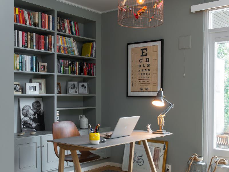 Bildet viser et lite hjemmekontor laget til i et ledig hjørne i en leilighet. En pult med PC og en lampe lyser ut i rommet. 