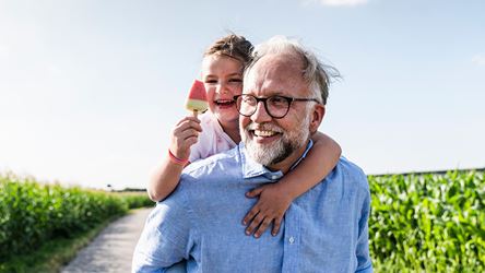 Bilde av en Bestefar med barnebarn på skuldrene ute på tur i grønne omgivelser.