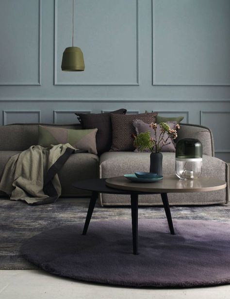Et interiørbildet med en brun sofa mot en grågrønn vegg. Lilla teppe på gulvet og et brunt rundt bord.