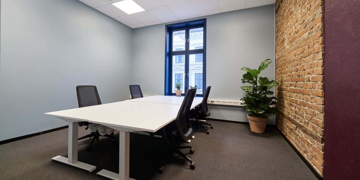 Bildet viser et kontorlokale i Thon Flex, Karl Johans gate 5. Den ene veggen har lys blå farge, ellers har veggene en dyp lilla farge med innslag av murstein. Hvite kontorpulter med svarte stoler. Et stort vindu gir mye lys i lokalet.