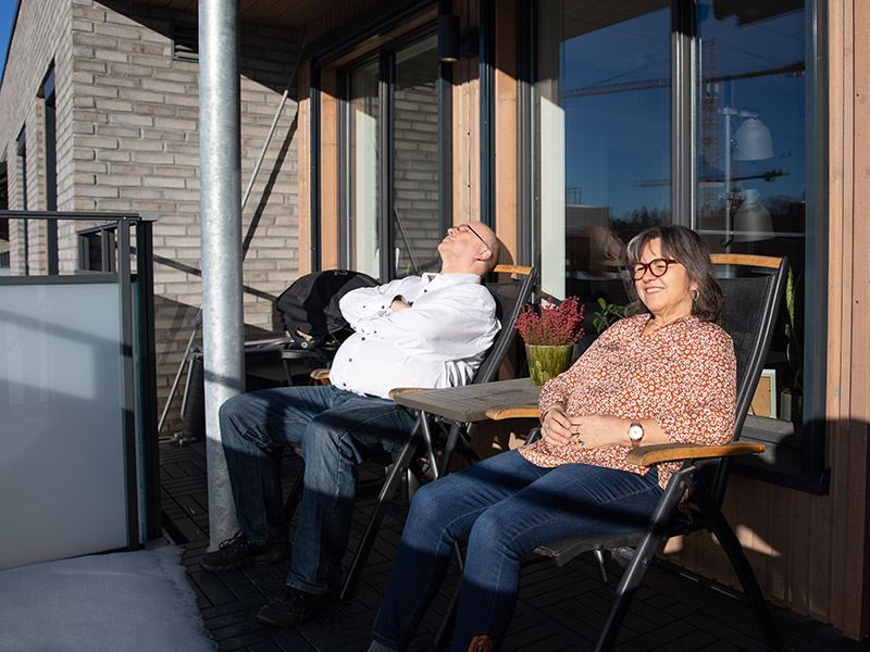 Bildet viser to personer som nyter solen på balkongen sin i boligprosjektet Skårerløkka på Lørenskog, rett utenfor Oslo.
