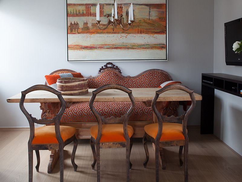 Bildet viser et spisestuebord i gammel stil. Mellombrunt bord med 6 stoler rundt. Stolene er i mørkt tre med oransje setetrekk. På veggen bak spisestuen skimtes et bilde malt i oransje, hvitt og brunt.