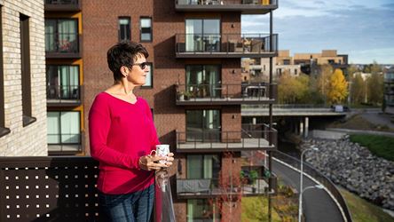 Bildet viser en dame i rød genser som står på balkongen sin i boligprosjektet Strømmen Verksted.